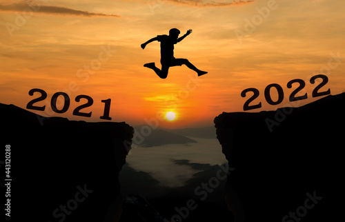 A young man jump between 2021 and 2022 years over the sun and through on the gap of hill silhouette evening colorful sky. happy new year 2022