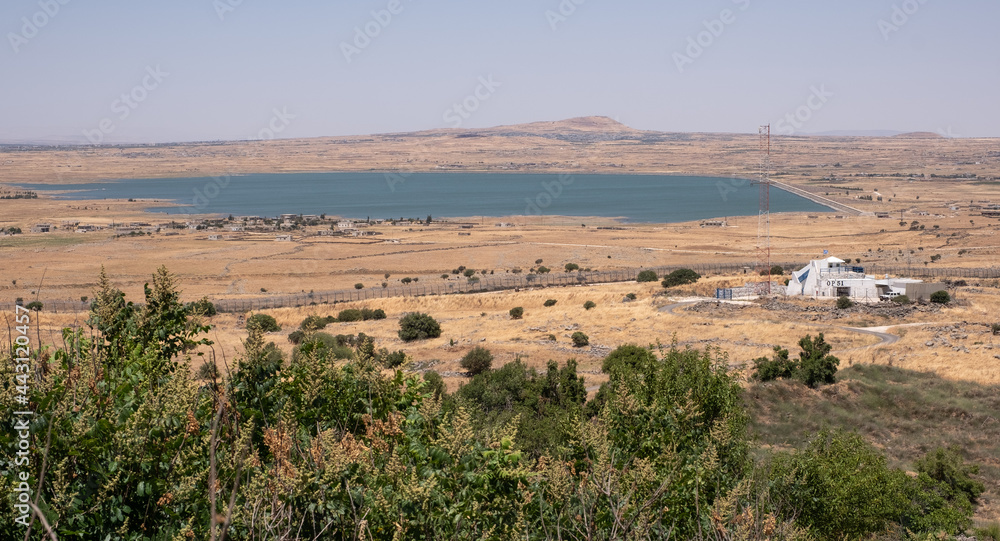 The fence of the border between Israel and Syria as seen from a hill on the Golan Heights. A building of the United Nation on the Israeli side and an abandoned village and a lake on the Syrian side. 