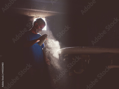 Man in respirator with paint spray can coloring board in darknes photo