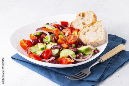 spanish salad with red beans and vegetables in a white plate, blue napkin, tomatoes, cucumbers, onions, ciabatta
