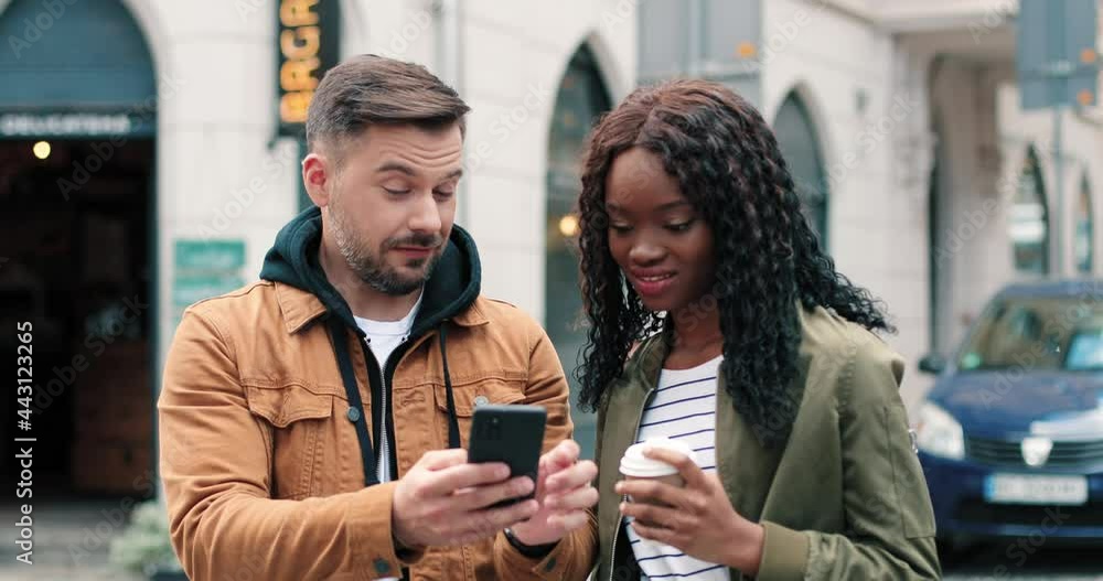 Look at this. Waist up portrait of the handsome bearded man explaining something to his multiracial female friend while looking at the smartphone. Friendship concept Look at this. Waist up portrait of the handsome bearded man explaining something to his multiracial female friend while looking at the smartphone. Friendship concept