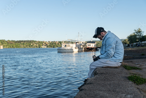 Young depressed suicidal drunk homeless man sitting under the bridge drinking alcohol drink and thinking to jump in to the river to commit suicide and end his life, social documentary concept