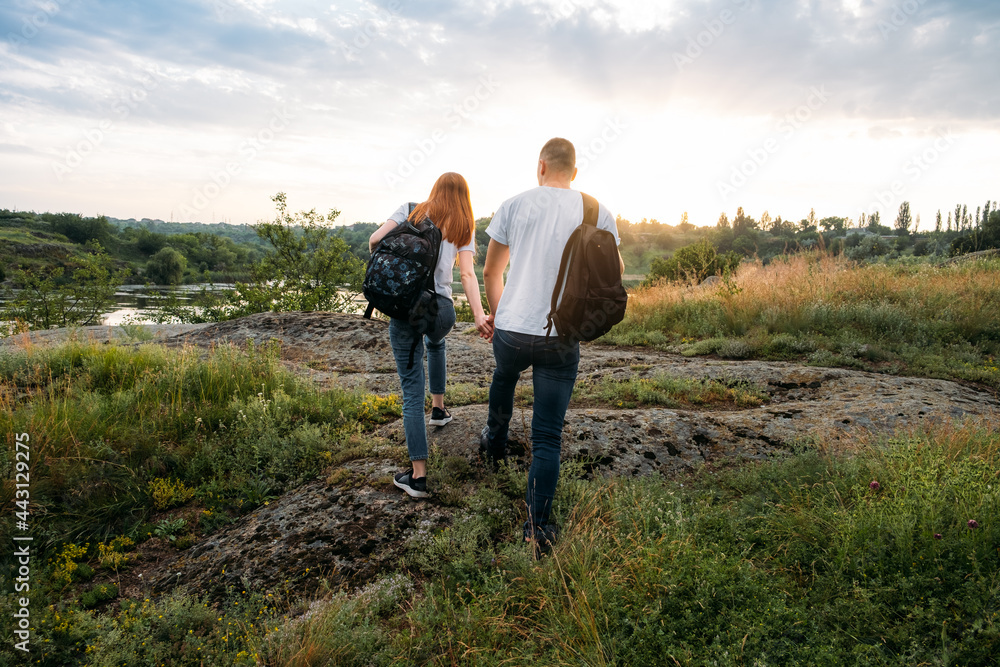 Adventure, Hiking, Trekking, Bushcraft Concept. Solo family travel. Local travel. Young happy couple travelers hiking with backpacks on rocky trail on sunset evening.