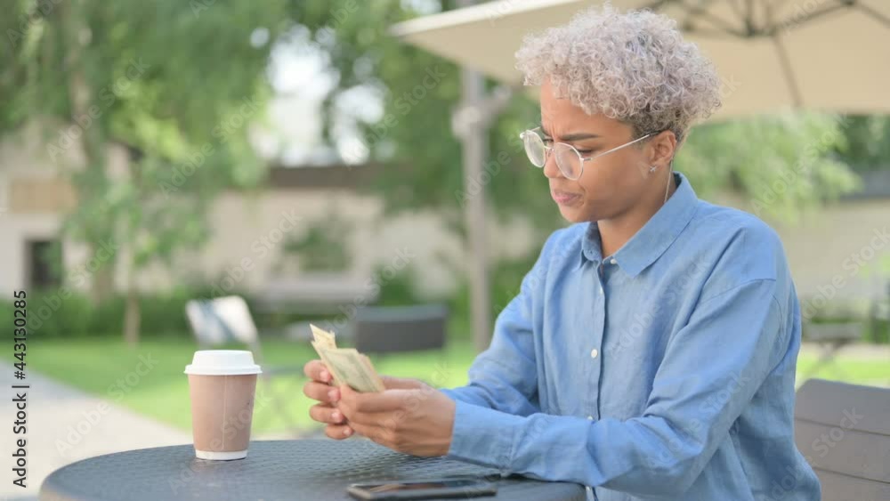 Young African Woman Feeling Sad while Counting Dollars in Outdoor Cafe Young African Woman Feeling Sad while Counting Dollars in Outdoor Cafe