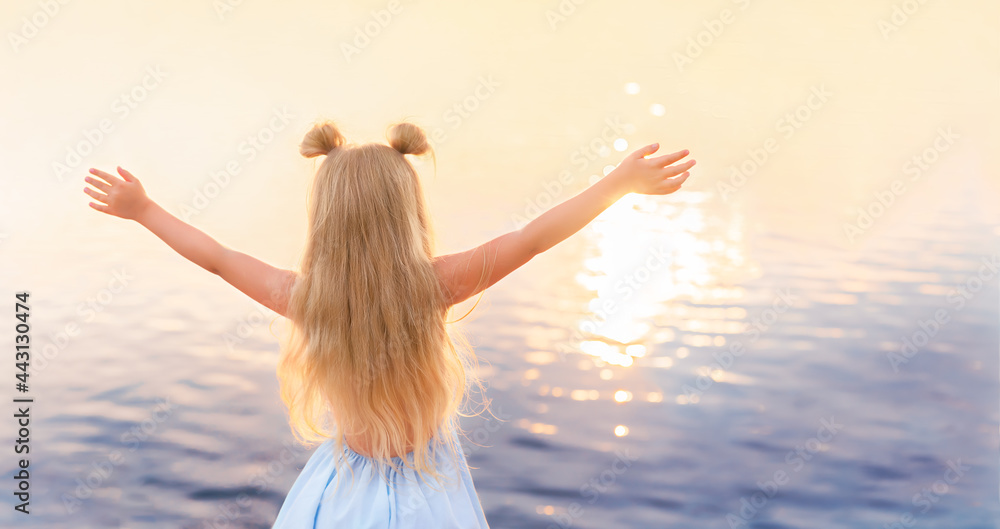 Little girl in the blue dress standing with raised arms at beautiful sunset on the sea. Soft focus.
Little girl in the blue dress standing with raised arms at beautiful sunset on the sea. Soft focus.