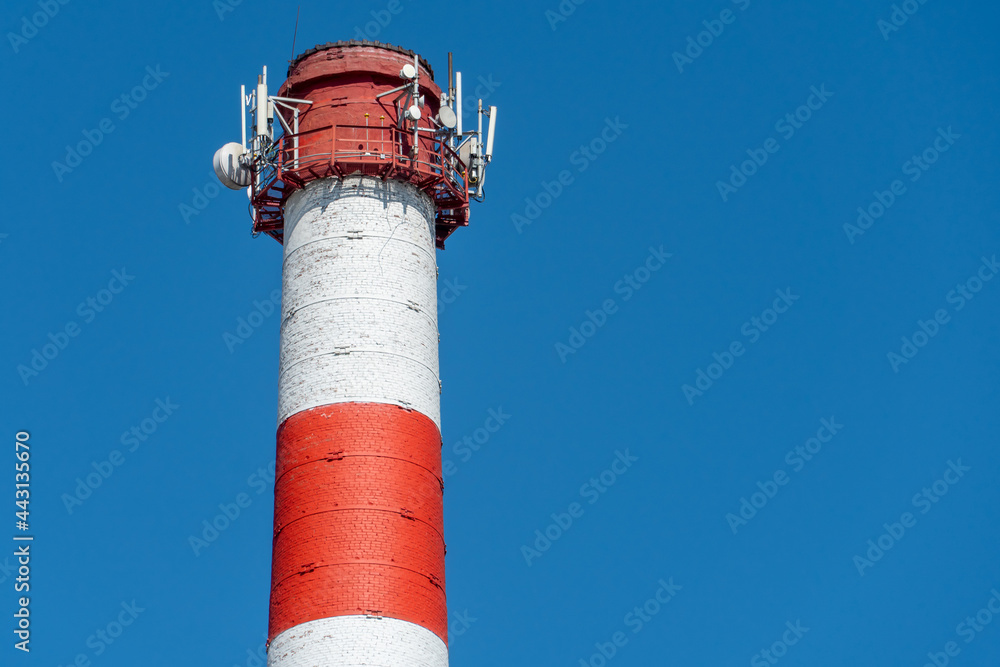 A large industrial smokestack against a blue sky. Red and white pipe in commercial enterprises or power plants. A large industrial smokestack against a blue sky. Red and white pipe in commercial enterprises or power plants.