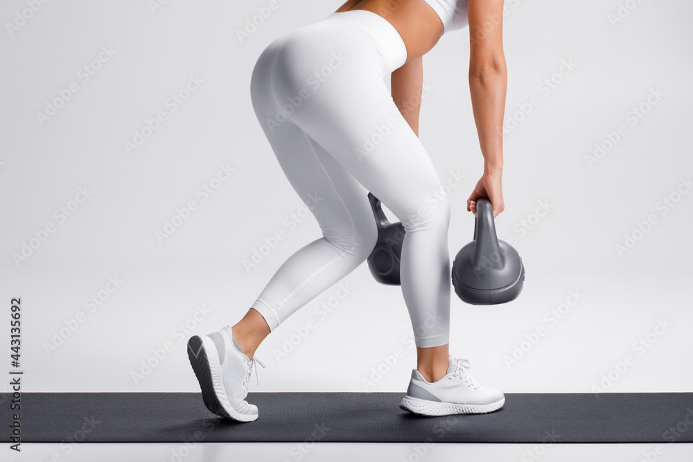 Athletic woman doing deadlift exercise for glutes on gray background. Fitness girl working out with kettlebells