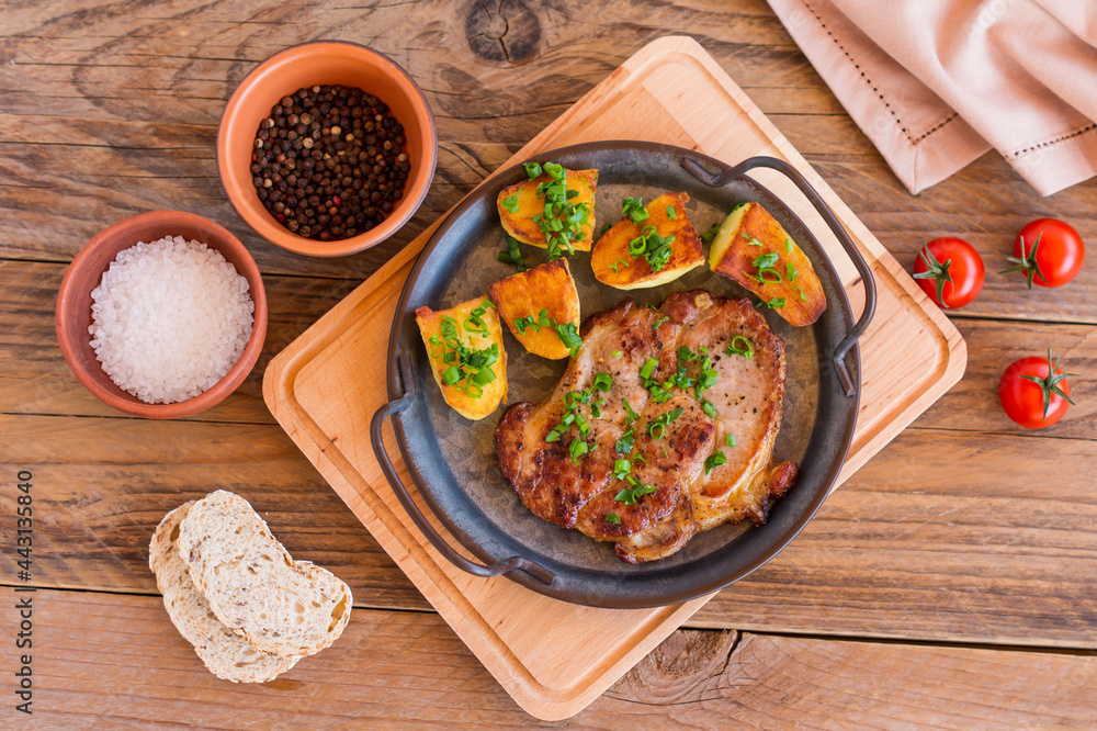 Roasted pork steaks in frying pan from neck meat with potato. wooden background. Roasted pork steaks in frying pan from neck meat with potato. wooden background.