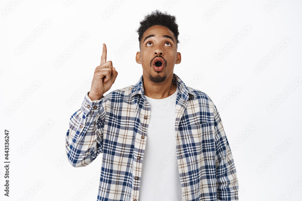 Surprised Black man gasping in awe, pointing and staring up at promo text, showing sale advertisement, being impressed, standing over white background Surprised Black man gasping in awe, pointing and staring up at promo text, showing sale advertisement, being impressed, standing over white background