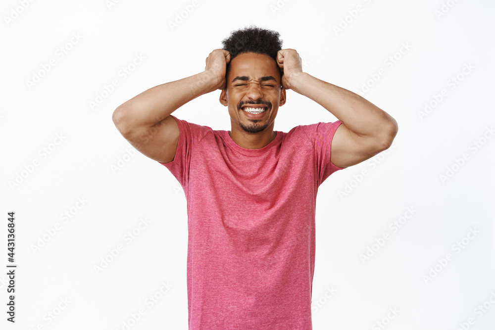 Frustrated african american guy holding hands on head, clench teeth and look distressed, bothered and annoyed by smth, feel complicated, standing against white background Frustrated african american guy holding hands on head, clench teeth and look distressed, bothered and annoyed by smth, feel complicated, standing against white background