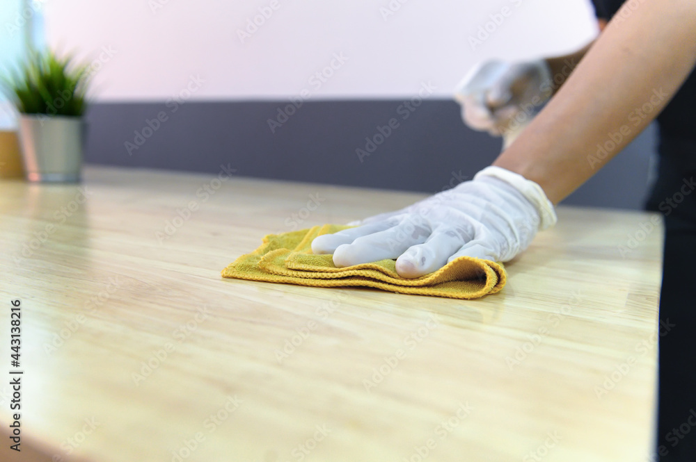 Hand of waiter woman cleaning table with disinfectant spray and microfiber cloth for disinfecting at indoor restaurant. Coronavirus prevention concept.