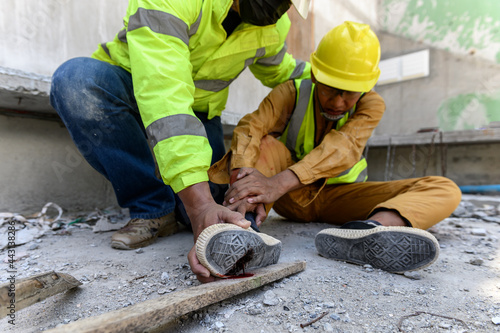 Builder worker has an accident at work. His feet stepped on nails embedded in wood old with foreman rushed in to take care. First aid and Safety in work concept. photo