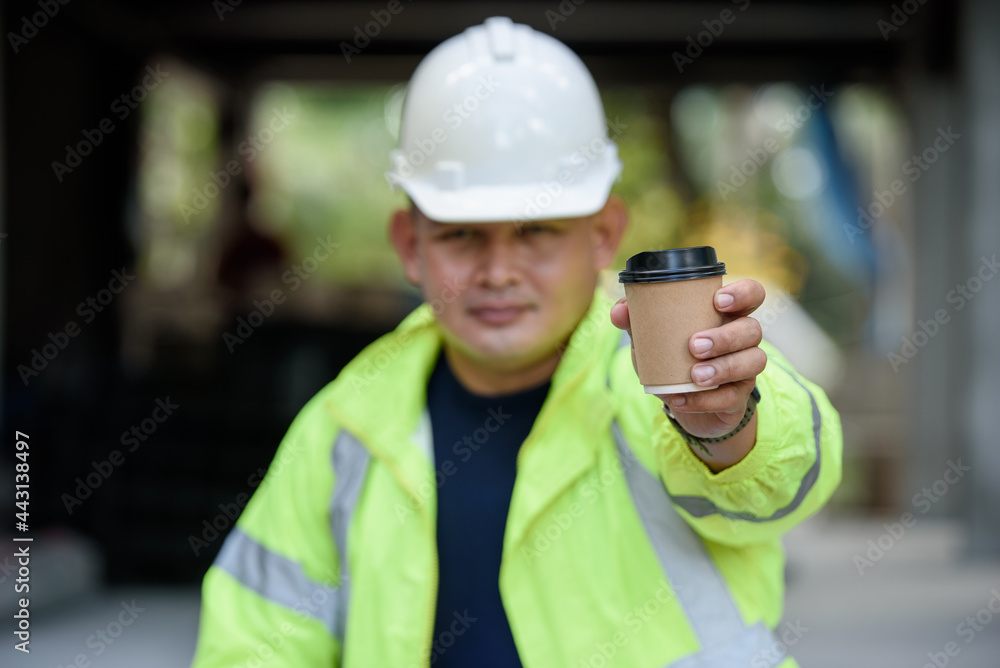 Construction engineer in reflective unifrom holds a cup hot coffee and hand to camera before work begins. Selection focuses on the cup of coffee. Construction engineer in reflective unifrom holds a cup hot coffee and hand to camera before work begins. Selection focuses on the cup of coffee.