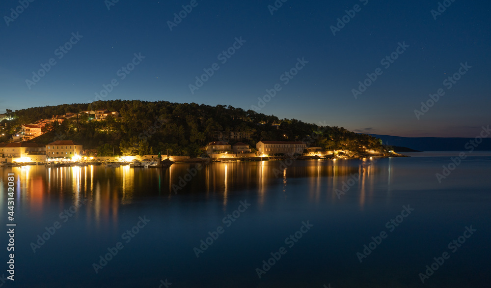 Night view of a very calm sea by the shore with a beautifully lit town in the background
