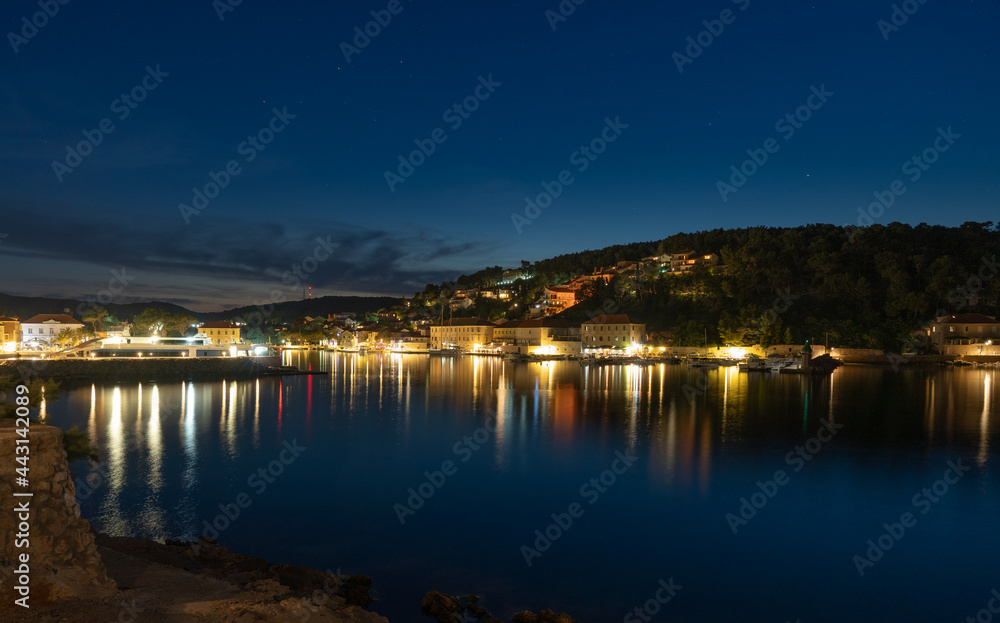 Night view of a very calm sea by the shore with a beautifully lit town in the background
