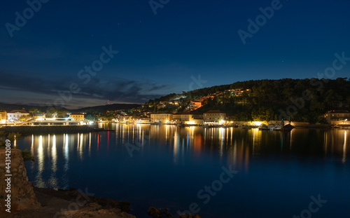 Night view of a very calm sea by the shore with a beautifully lit town in the background