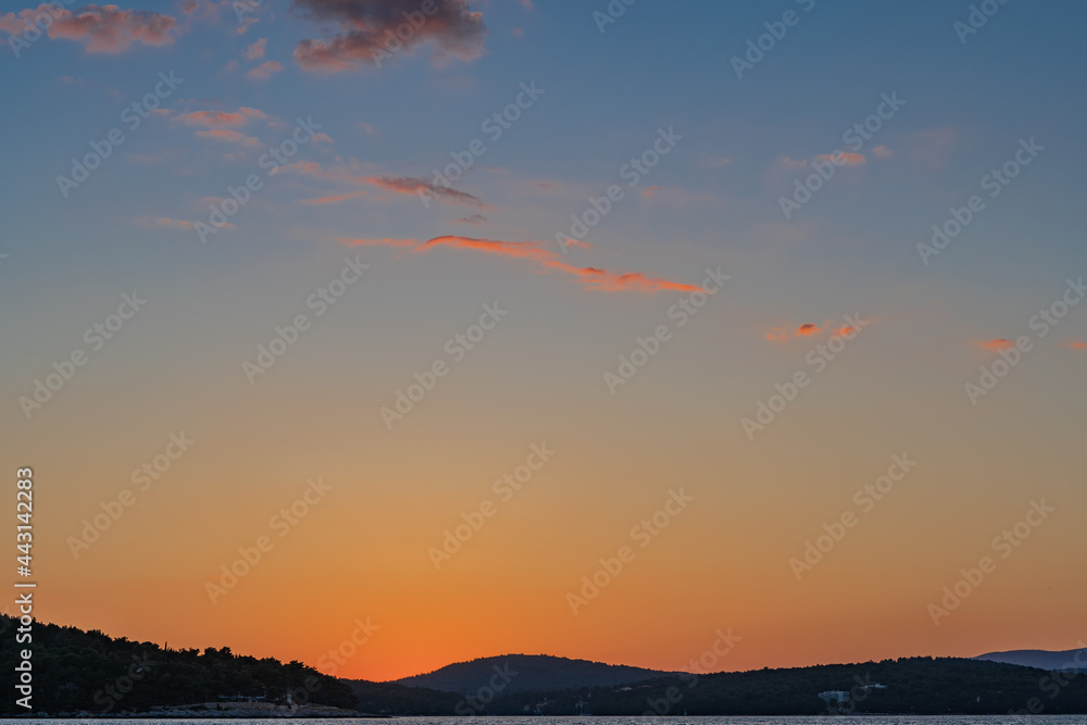 Fototapeta premium The sun just above the sea horizon creating a sunrise / sunset with a panorama of the mountains and rocky beaches