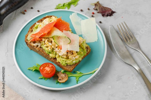 Toast with scrambled eggs, avocado, smoked salmon and vegetables on rye bread. On a blue plate, horizontal
