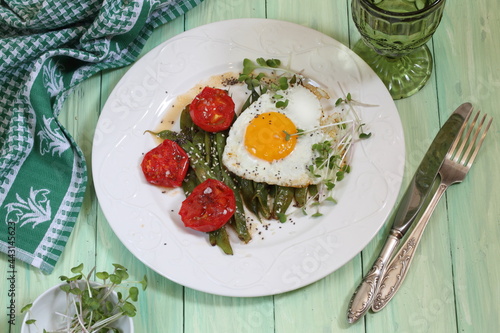 Scrambled eggs with tomatoes and green beans on green wooden background
