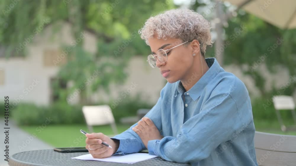 Young African Woman Writing on Paper in Outdoor Cafe Young African Woman Writing on Paper in Outdoor Cafe