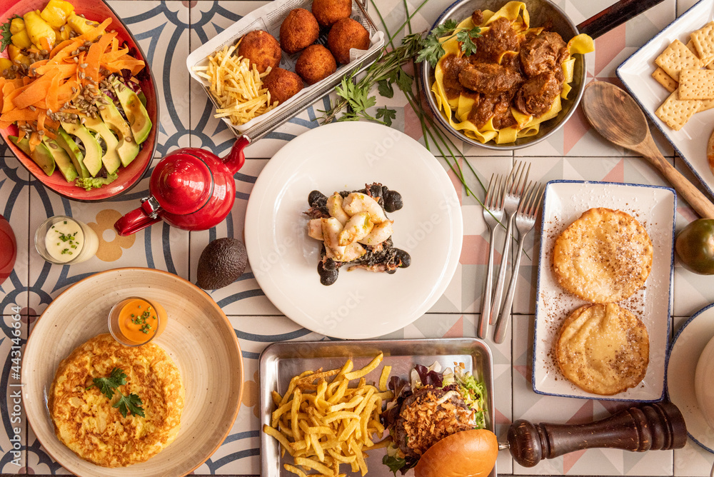 top view image of typical dishes of Spanish gastronomy. Iberian ham croquettes, stewed pork cheek, potato tortilla, Squid in ink. top view image of typical dishes of Spanish gastronomy. Iberian ham croquettes, stewed pork cheek, potato tortilla, Squid in ink.