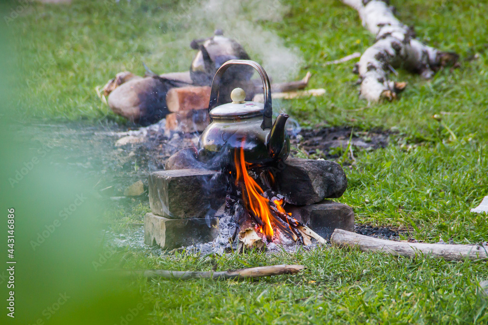 Fototapeta premium Metallic kettle on the bricks above bonfire - picnic scene