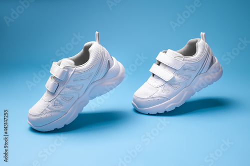 side view white unisex sneakers with velcro fasteners fly in air and simulate walk or run isolated on a blue background. photo