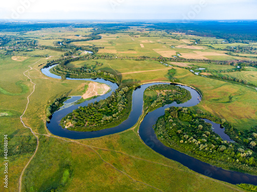 Aerial view of a curve river among fields and forests with town on the horizon