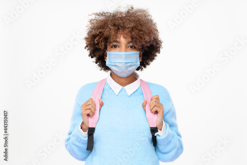 Studio portrait of african american school girl or college student with curly afro hair wearing medical mask, isolated on gray background © Damir Khabirov