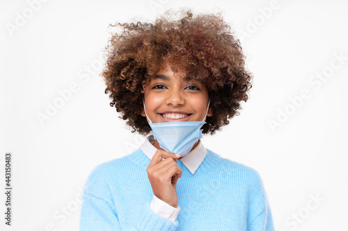 Portrait of smiling african american school girl taking off face mask after the end of pandemic. Concept of future, hope and recovery. Covid virus defeated, people are getting back to normal life © Damir Khabirov