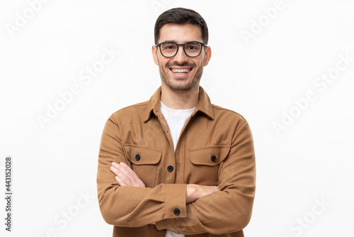 Portrait of young happy laughing man wearing brown shirt and eyeglasses, holding arms crossed, isolated on gray background