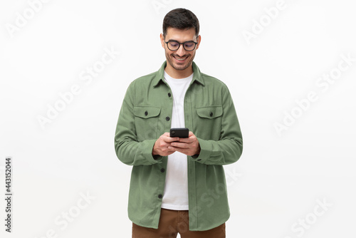 Young man in green casual shirt looking at phone, standing isolated on gray background photo