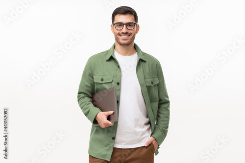 Smiling modern businessman looking at camera through glasses, holding laptop, isolated on gray background