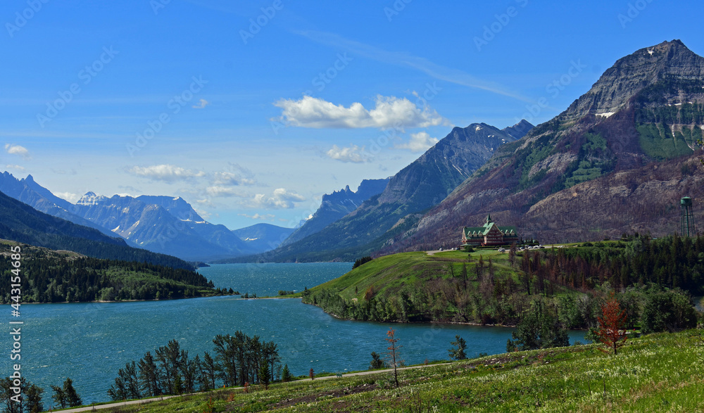 the spectacular view on a sunny day across turquoise-colored waterton lakes to prince of wales hotel  in waterton, alberta, canada, to  the peaks of glacier national park, montana