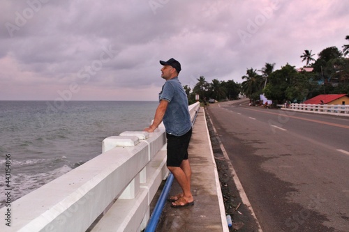 A man standing on a bridge against a gray sky and raging sea and looking into the distance