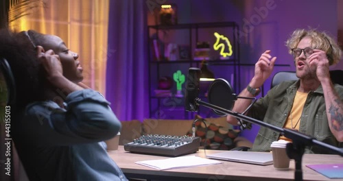 Bye. Waist up portrait view of the young multiracial woman and caucasian man sitting together at the desk in recording studio with neon light while saying bye and smiling at each other photo