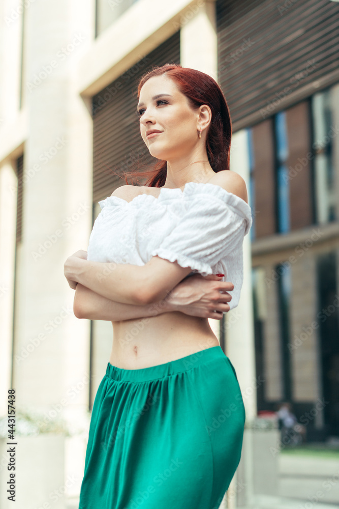 Portrait of thirty years old red-haired girl in the summer against the background of a modern building
