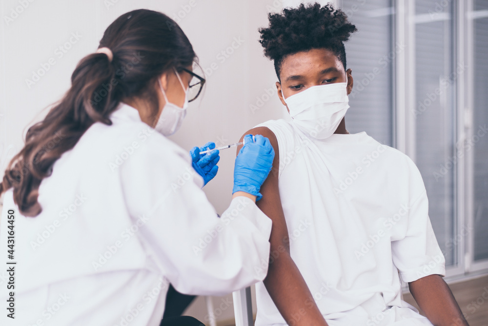 Naklejka premium African boy wearing face mask getting vaccinated during coronavirus or covid-19 pandemic at hospital,Vaccination concept