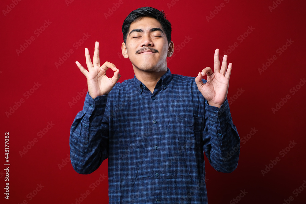Young indian man wearing casual shirt relax and smiling with eyes closed doing meditation gesture with fingers. Yoga concept. Young indian man wearing casual shirt relax and smiling with eyes closed doing meditation gesture with fingers. Yoga concept.