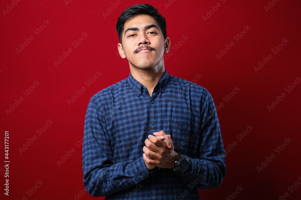Fototapeta premium Young handsome man wearing casual shirt with hands together and crossed fingers smiling relaxed and cheerful. Success and optimistic