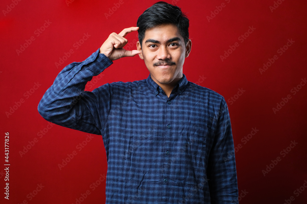 Young handsome man wearing casual shirt smiling and confident gesturing with hand doing small size sign with fingers looking and the camera. measure concept.