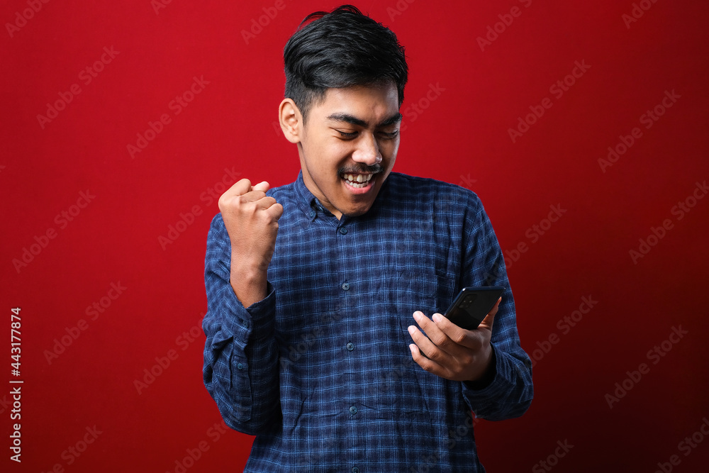 Young indian man using smartphone screaming proud and celebrating victory and success very excited, cheering emotion Young indian man using smartphone screaming proud and celebrating victory and success very excited, cheering emotion