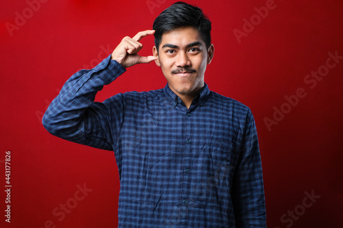 Young handsome man wearing casual shirt smiling and confident gesturing with hand doing small size sign with fingers looking and the camera. measure concept. © Reza