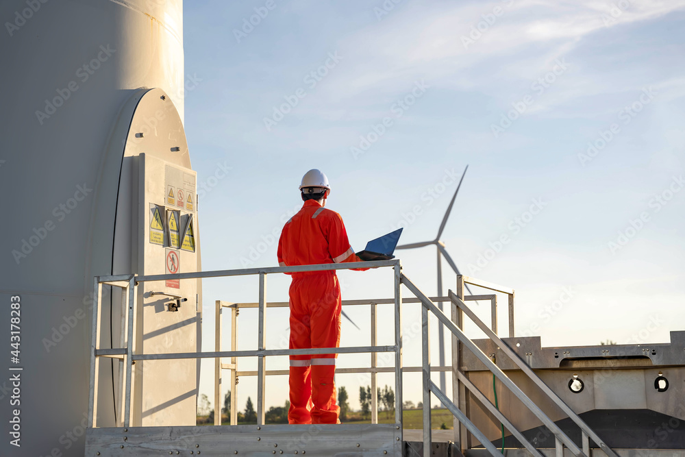 Man engineer working and holding the laptop for check performance of wind turbine farm Power Generator Station, Concept of sustainable resources, Concept of professional for the energy industry Man engineer working and holding the laptop for check performance of wind turbine farm Power Generator Station, Concept of sustainable resources, Concept of professional for the energy industry