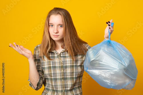 Waste sorting and sustainability concept - sad young woman holding plastic trash bag over yellow background.