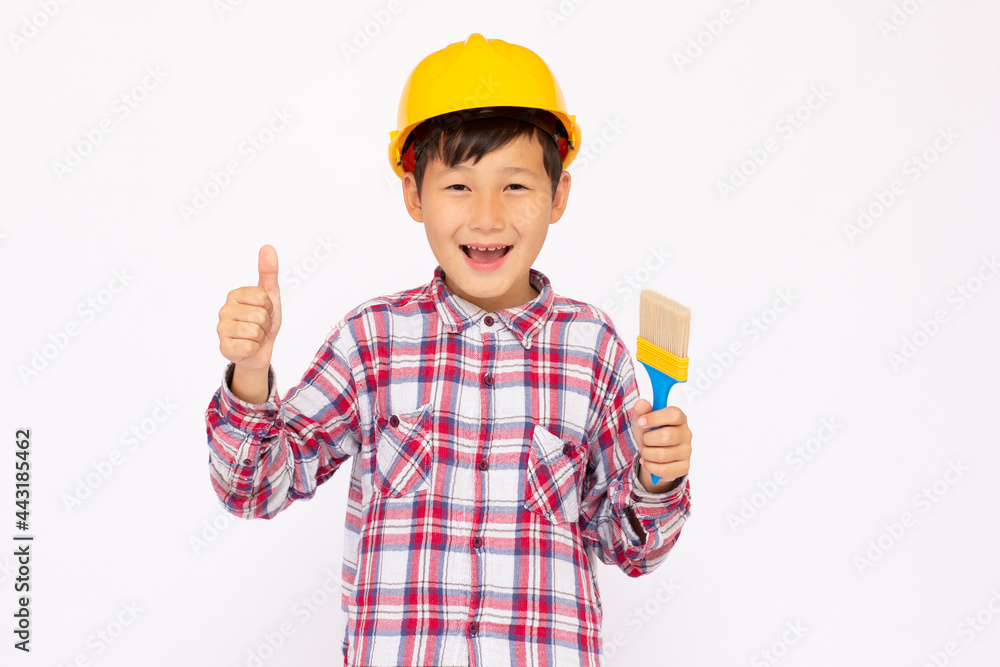 Little kid as a construction worker wearing yellow helmet with a paintbrush in his hand..White background studio picture. Little kid as a construction worker wearing yellow helmet with a paintbrush in his hand..White background studio picture.