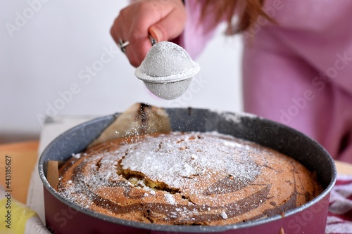 Woman's hand sprinkling icing sugar over fresh sponge cake. Powder sugar falls on fresh perfect marble cake/ Recipes and ideas for breakfast cake