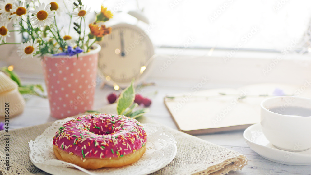 Donut in pink glaze on a background of wild flowers of chamomiles, fresh berries on a wooden table Donut in pink glaze on a background of wild flowers of chamomiles, fresh berries on a wooden table
