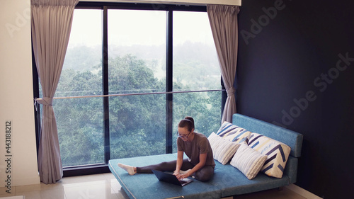 Girl freelancer works for a laptop while lying on a sofa near the window. Free work in the home