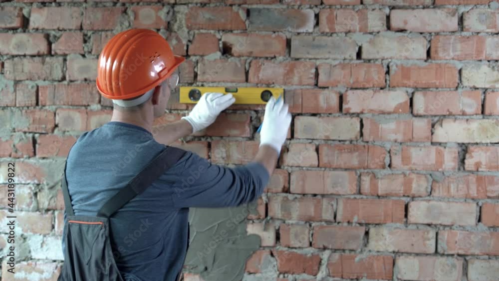 a Caucasian male builder dressed in a uniform and an orange hard hat on ...